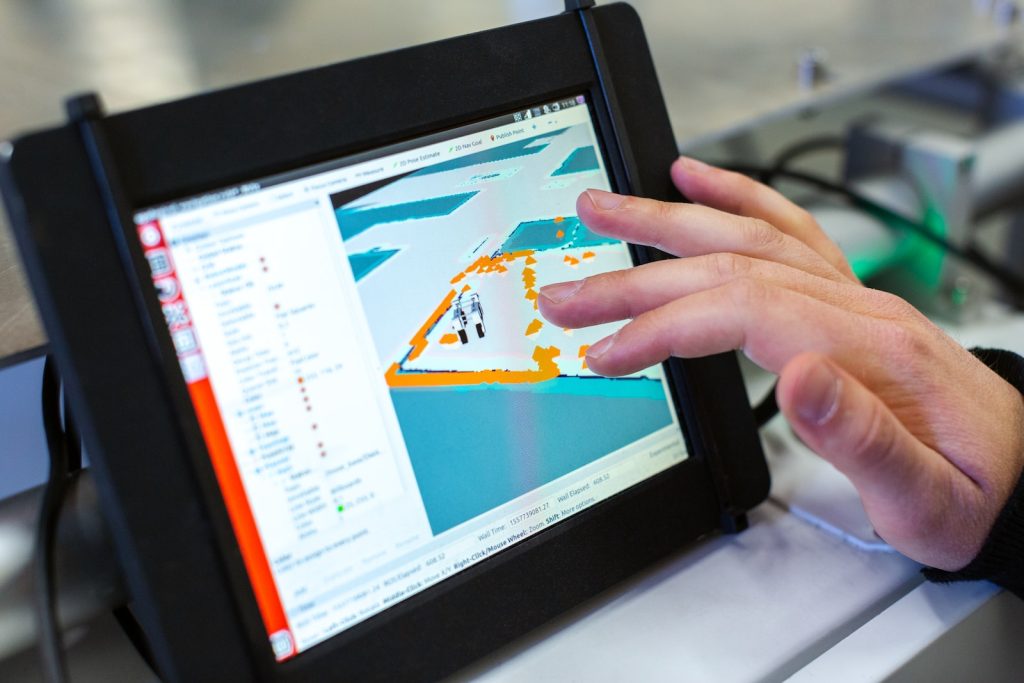 Touchscreen displaying digital map; hand interacting with location software in a tech environment.